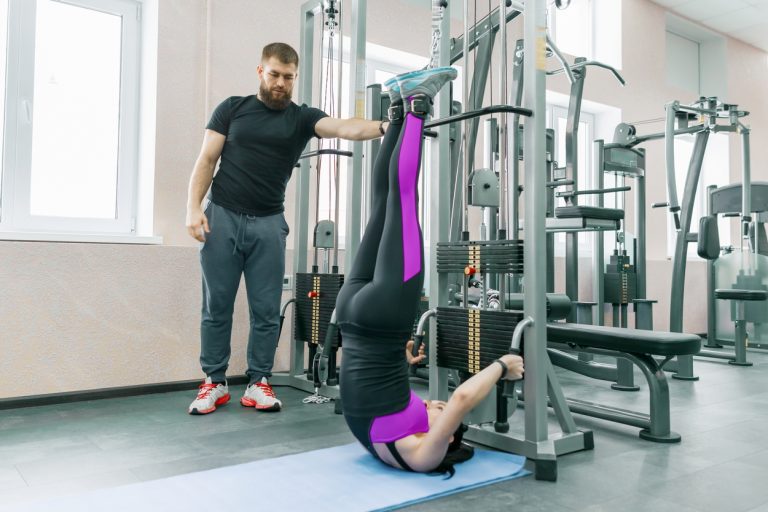 Kinesis technology, kinesitherapy, healthy lifestyle. Young woman doing rehabilitation exercises with personal instructor using kinesi machine.
