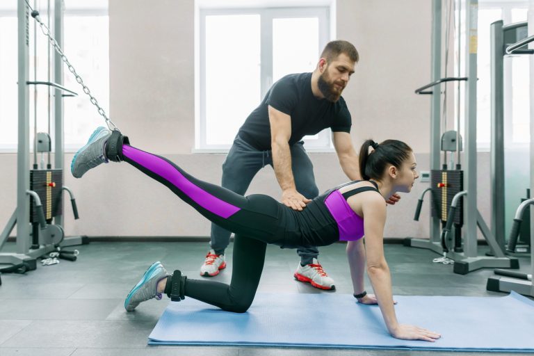 Kinesis technology, kinesitherapy, healthy lifestyle. Young woman doing rehabilitation exercises with personal instructor using kinesi machine.
